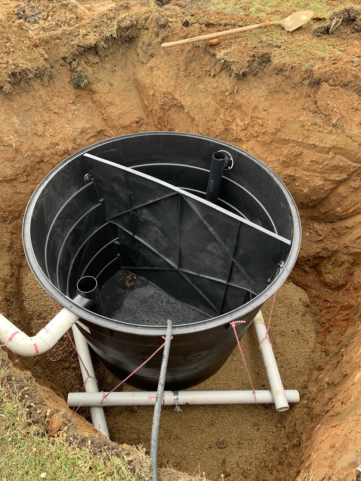 A septic tank set into a freshly dug hole with the pipework connected