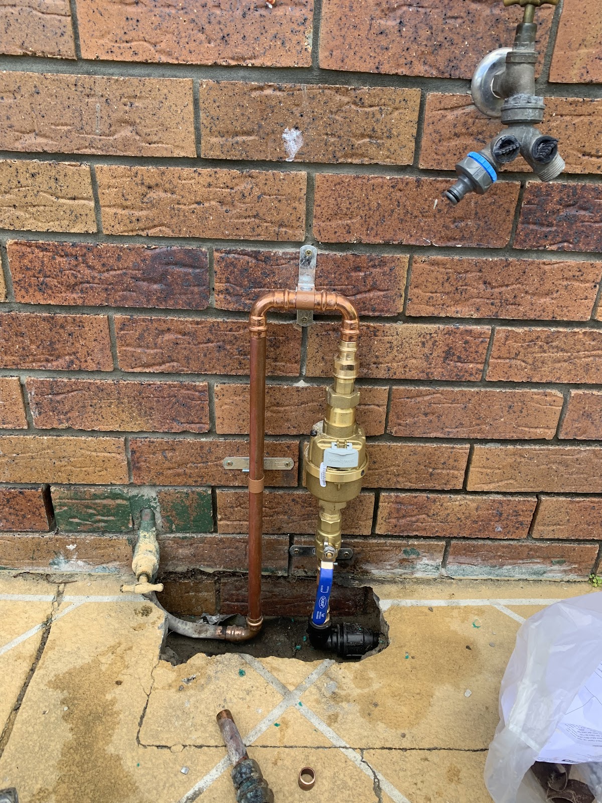 New copper pipe riser with a brass water meter and blue isolation valve against a brick wall
